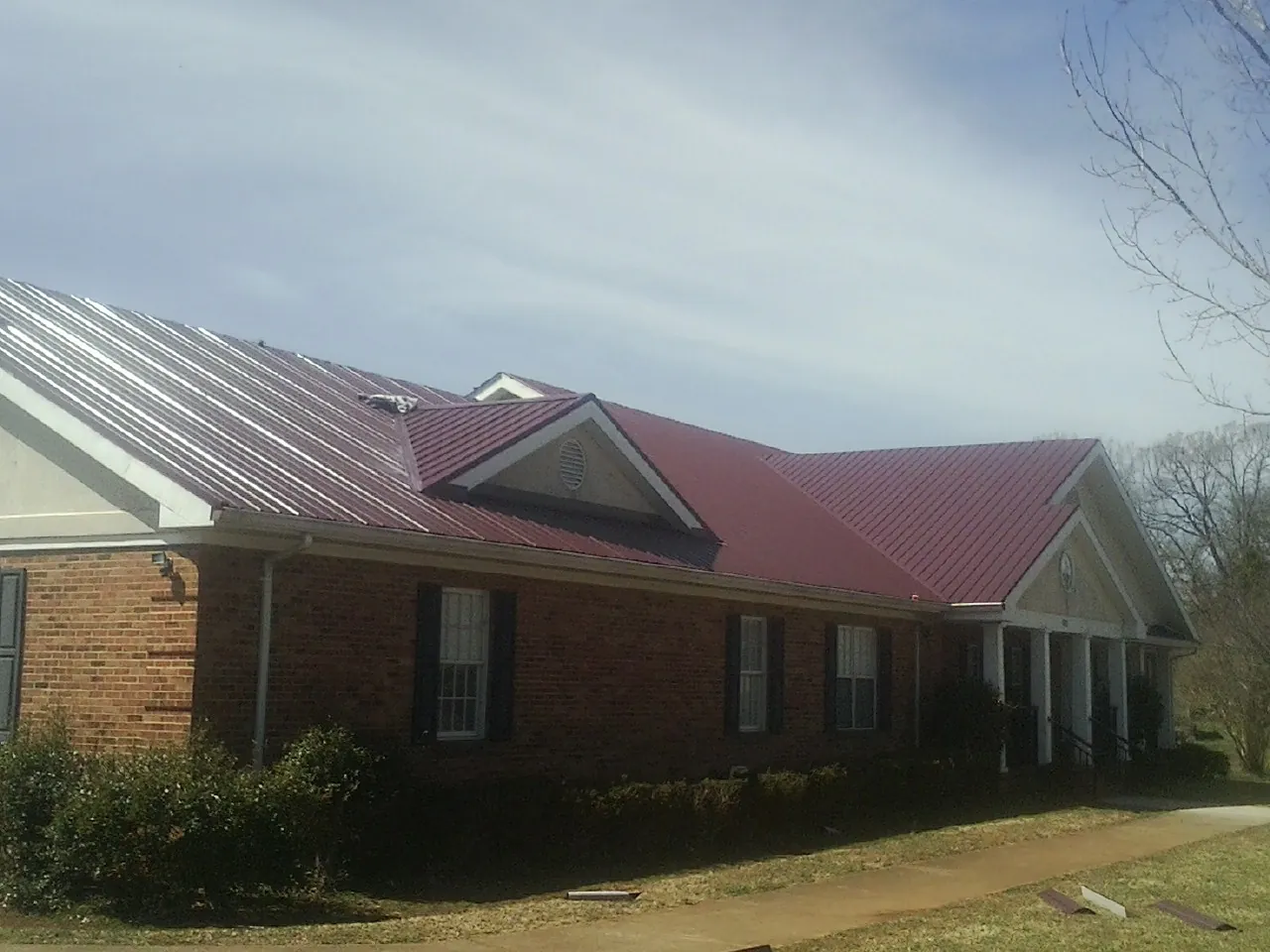 Red metal roof with gabled entries on a long brick building, from a Hail Damage Roof Repair job in Cambridge